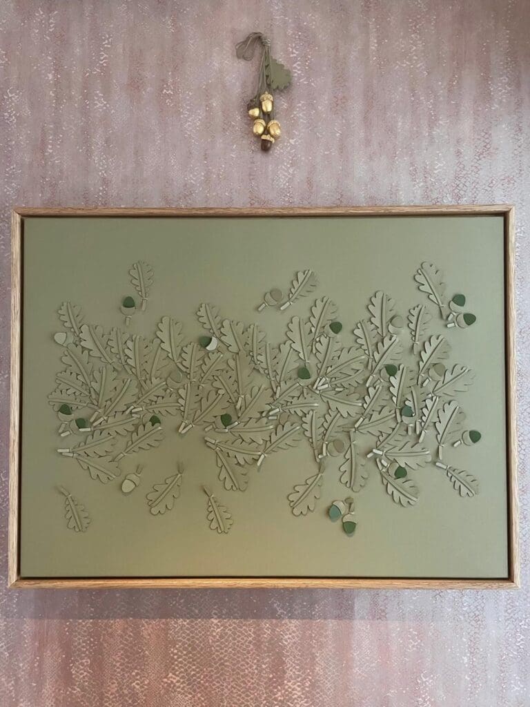 Green leather oakleaf artwork with cluster of gilded acrons hung above